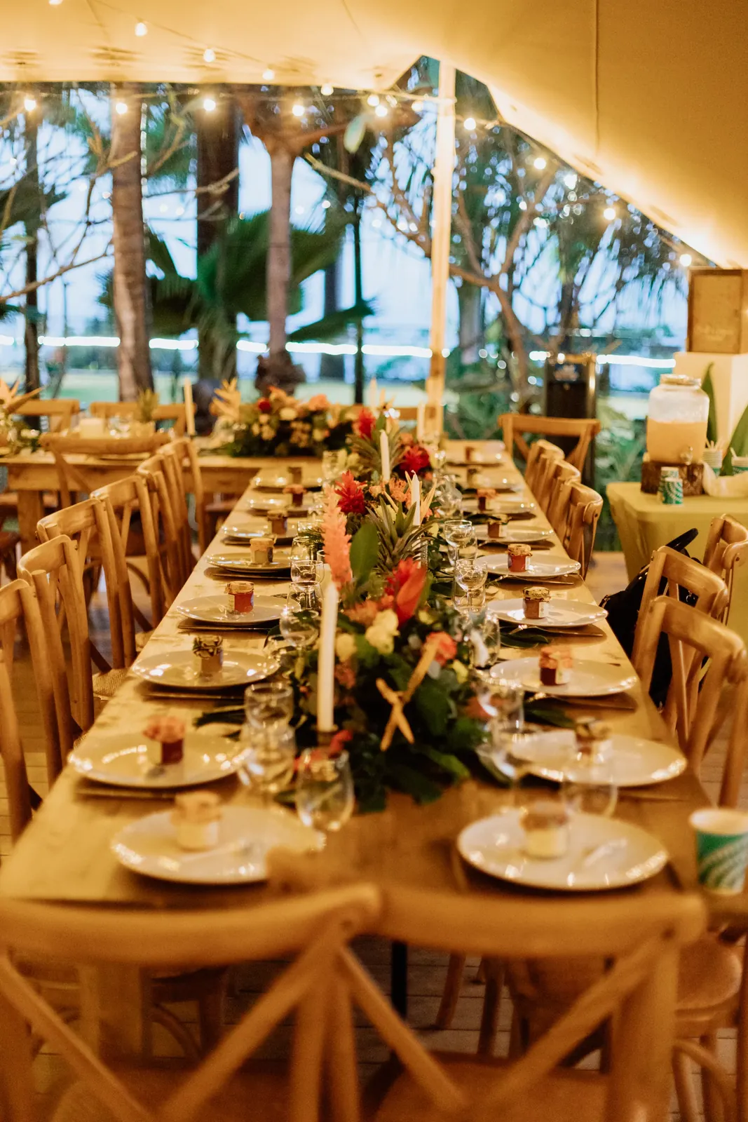 Longue tablée de mariage sous tente, bouquets de fleurs tropicales et bougies